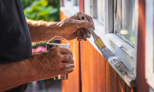 Mann lackiert alte Holzfensterrahmen neu in weiß