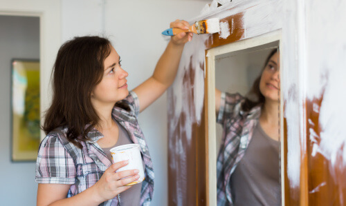 Junge Frau lackiert einen alten Schrank mit Spiegeltür neu in weiß